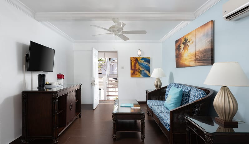 One Bedroom Pool Garden View Suite living room with blue sofa, TV cabinet, and dark tiled flooring at The Club Barbados Resort & Spa by Kenwood Travel