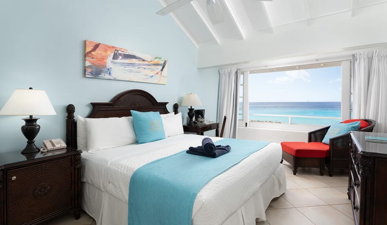 Ocean Loft Ocean View bed with a turquoise runner and a view of the ocean through a large window at The Club Barbados Resort & Spa by Kenwood Travel