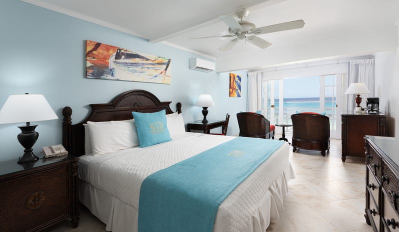 Superior Garden View bedroom with dark wood furnishings and an ocean view balcony at The Club Barbados Resort & Spa by Kenwood Travel