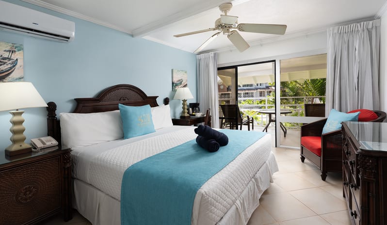 Garden View light blue walls, dark wood bed frame, and private outdoor balcony at The Club Barbados Resort & Spa-Garden View by Kenwood Travel