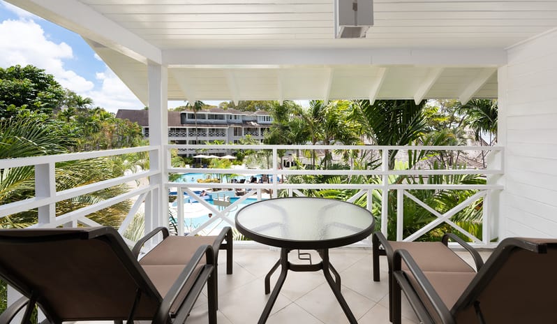 Garden View balcony with glass table and lounge chairs overlooking a resort pool at The Club Barbados Resort & Spa-Garden View by Kenwood Travel