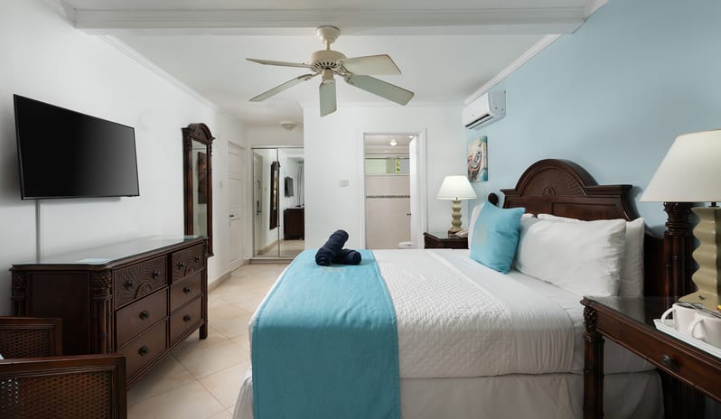 Garden View bedroom with flat-screen TV, dark wood furniture, blue accent wall, and ceiling fan at The Club Barbados Resort & Spa-Garden View by Kenwood Travel