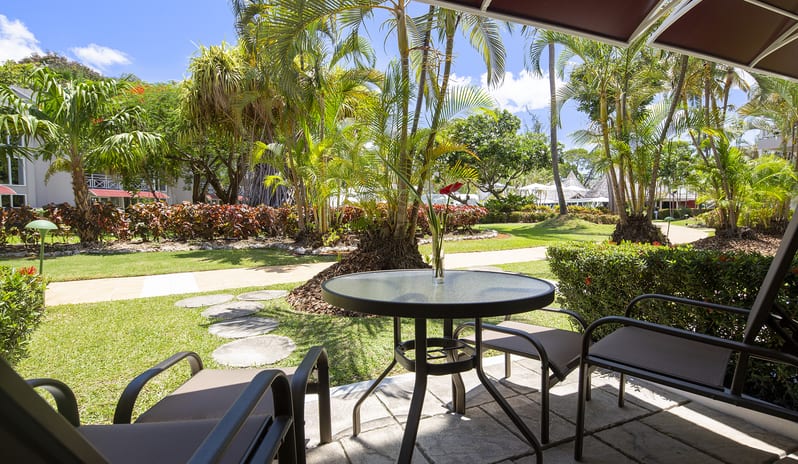 Garden View patio with glass table and chairs overlooking a sunny tropical garden at The Club Barbados Resort & Spa-Garden View by Kenwood Travel