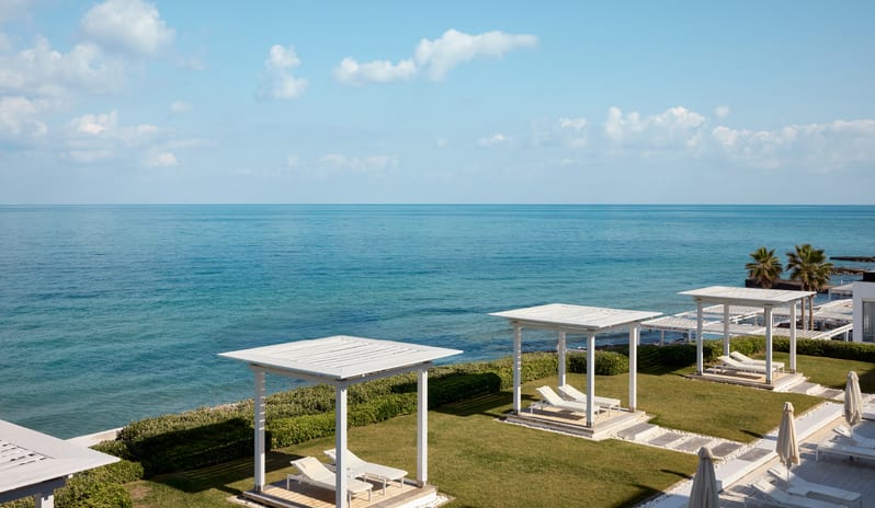 Grecotel LUXME White Prestige Guestroom Sea View Oceanfront white cabanas and lounge chairs along the coast-Kenwood Travel