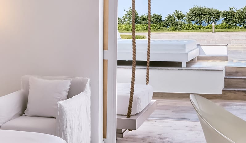 Prestige Guestroom Sea View minimalist interior opening onto a sun terrace with a rope-suspended swing seat and outdoor lounge daybed at Grecotel LUXME White by Kenwood Travel