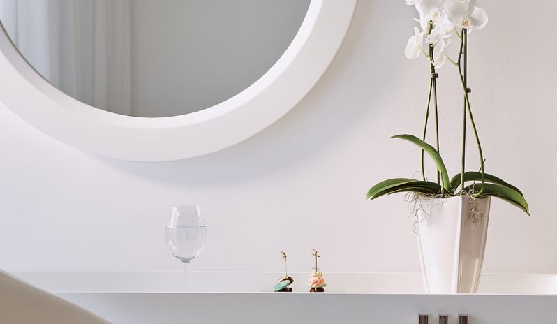 Swim-up Guestroom Sea View Potted white orchid on a modern white console table next to a round mirror at Grecotel LUXME White by Kenwood Travel