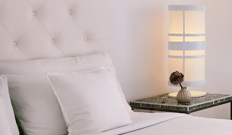 Prestige Guestroom Sea View Modern white tufted headboard next to a lighted bedside lamp. daybed at Grecotel LUXME White by Kenwood Travel