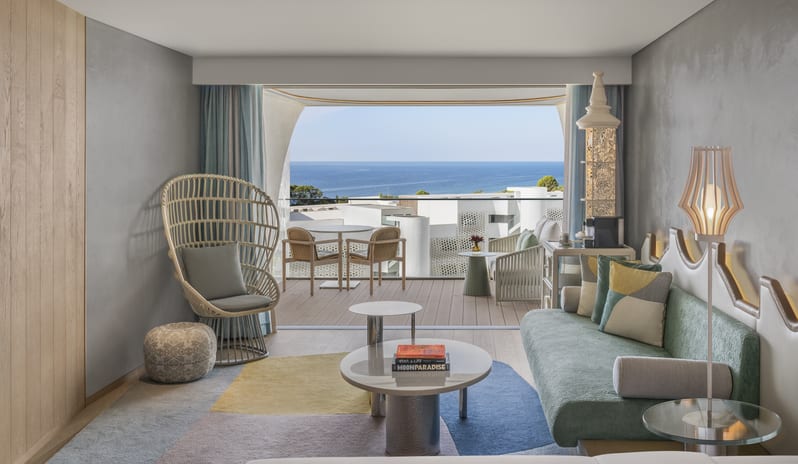 Premium Deluxe Room Modern luxury resort suite featuring a mint green sofa, woven lounge chair, and private balcony overlooking the ocean at W Algarve by Kenwood Travel