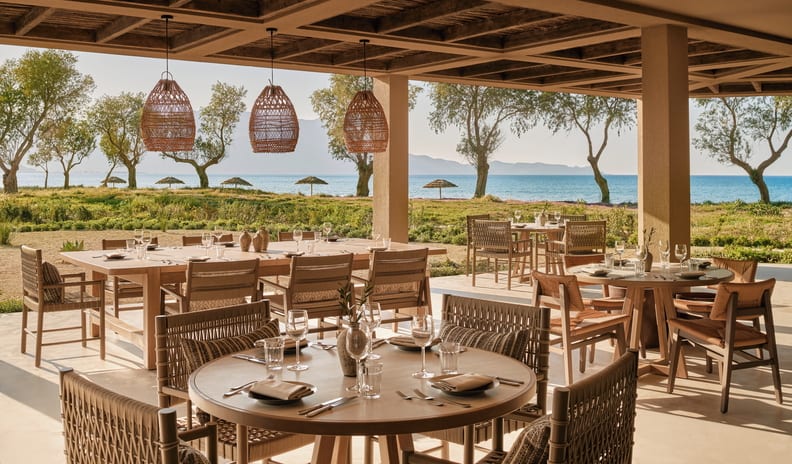 Kriti Luxury Mediterranean style beachfront resort dining patio featuring woven rattan pendant lights, wooden dining tables, and scenic ocean views at Ikos Kissamos by Kenwood Travel
