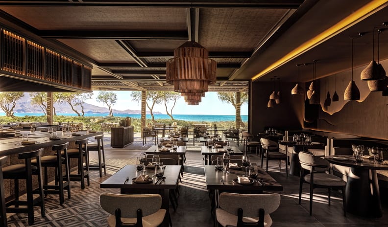AnayaLuxury Mediterranean style resort oceanfront restaurant interior with dark wooden tables, woven pendant chandeliers, and panoramic sea views at Ikos Kissamos by Kenwood Travel