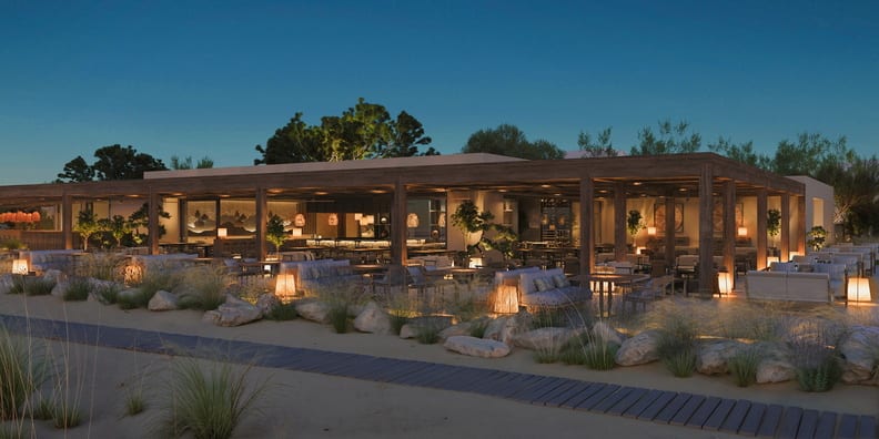 Anaya Luxury outdoor beachside restaurant at dusk featuring a large wooden pergola, warm woven lighting, comfortable lounge seating, and a wooden boardwalk path at Ikos Kissamos by Kenwood Travel