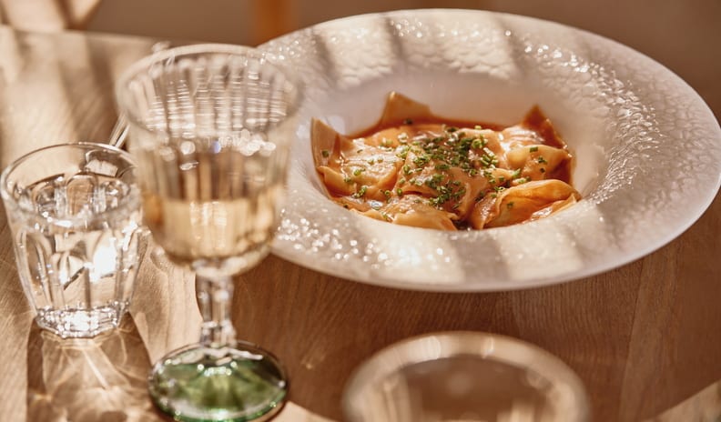 La Plage Gourmet handmade stuffed ravioli pasta garnished with fresh chives, served in a wide textured white bowl next to glasses of water and wine at Ikos Kissamos by Kenwood Travel