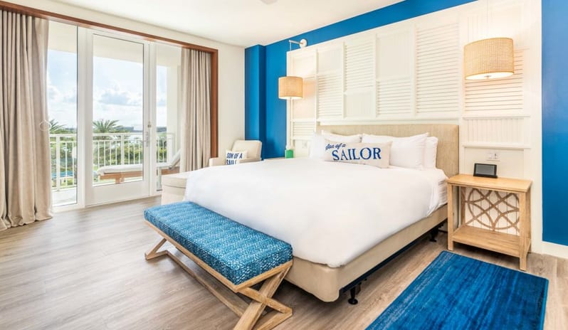 One Bedroom Suite Modern coastal bedroom suite featuring a king bed with white bedding, blue accent wall, shutter headboard, and sliding balcony doors  at Margaritaville Resort Orlando by Kenwood Travel
