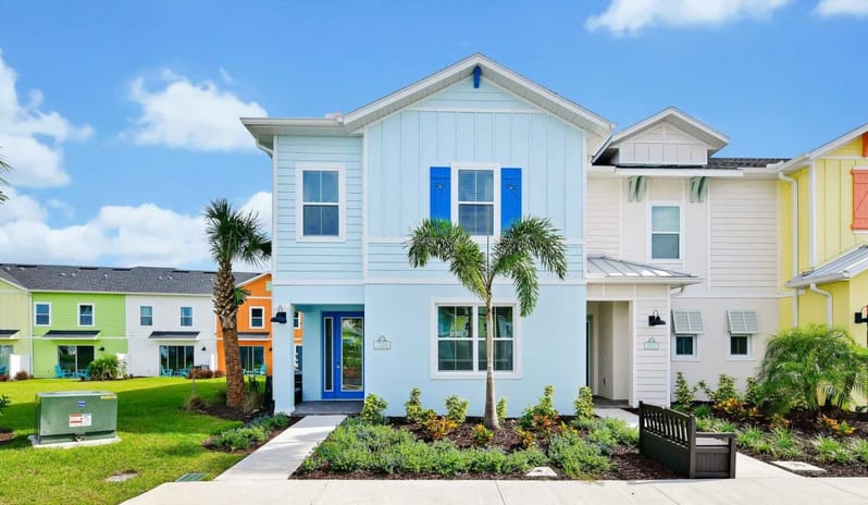 Two Bedroom Villa Two-story pastel blue coastal vacation home with dark blue shutters, a blue front door, palm trees, and a landscaped walkway at Margaritaville Resort Orlando by Kenwood Travel
