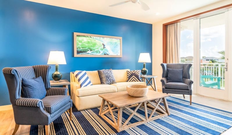 One Bedroom Suite Resort suite living room with stylish blue wingback chairs, cream sofa, patterned rug, and natural light at Margaritaville Resort Orlando by Kenwood Travel