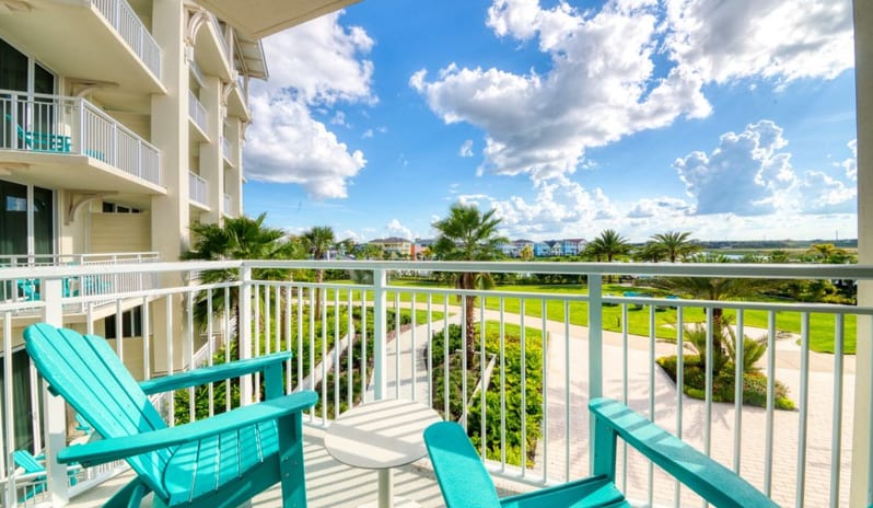 One Bedroom Suite View from a resort suite balcony with teal seating looking over landscaped gardens and palm trees at Margaritaville Resort Orlando by Kenwood Travel