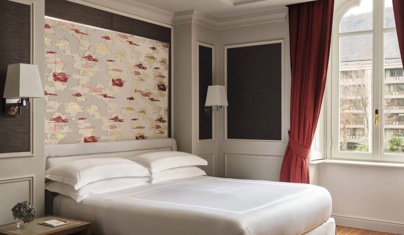 Premium Room Premium guest room bed with white linens next to a large window with red drapes at Palazzo Venezia by Kenwood Travel