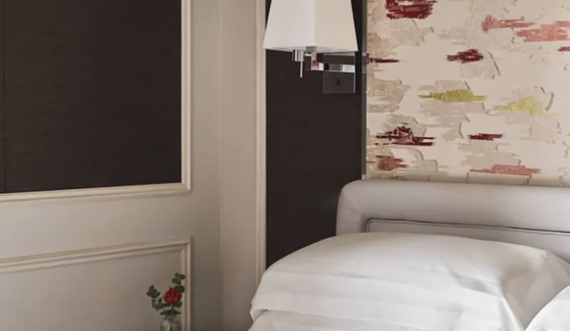 Standard Room Detail view of a luxury hotel bed with white embroidered linens next to a wall light at Palazzo Venezia by Kenwood Travel