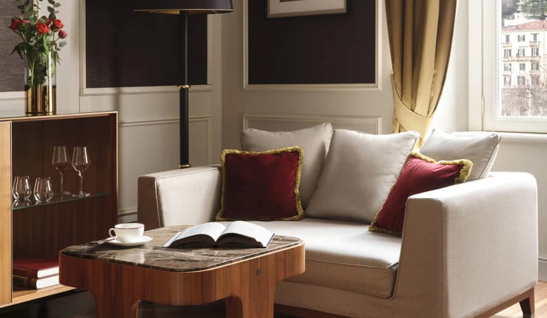 Junior Suite sitting area with a marble coffee table, open book, tea cup, black floor lamp, glassware cabinet, and herringbone parquet flooring at Palazzo Venezia by Kenwood Travel
