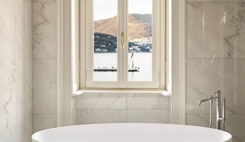 Suite Soaking tub in a white marble bathroom with an arched lake-view window at Palazzo Venezia by Kenwood Travel