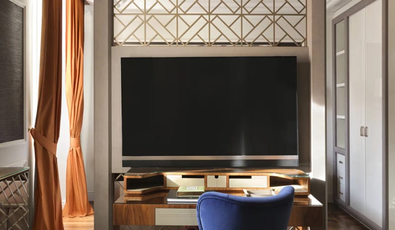 Deluxe Double Room room divider featuring a mounted TV screen and desk workstation with a blue chair at Palazzo Venezia by Kenwood Travel