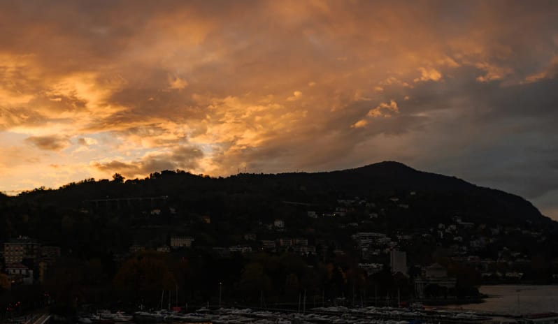 Altariva Bar Panoramic view of a golden orange sunset behind dark mountain silhouettes with docked boats in the lake marina below at Palazzo Venezia by Kenwood Travel