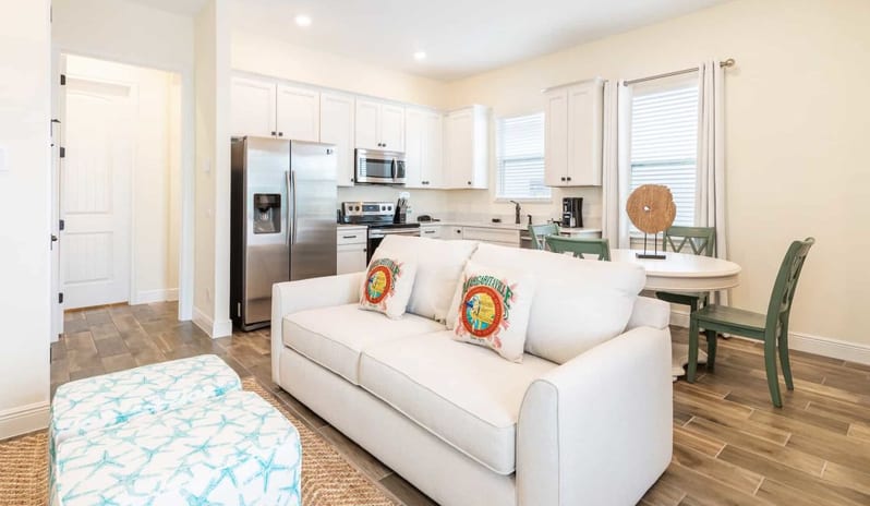 Two Bedroom Villa Bright open-plan living room with a white sofa and ottomans next to a kitchen and dining area at Margaritaville Resort Orlando by Kenwood Travel