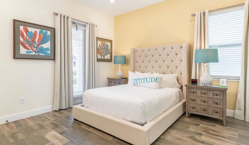 Two Bedroom Villa Modern bedroom with a high tufted headboard, white bedding, wooden nightstands, and blue bedside lamps at Margaritaville Resort Orlando by Kenwood Travel