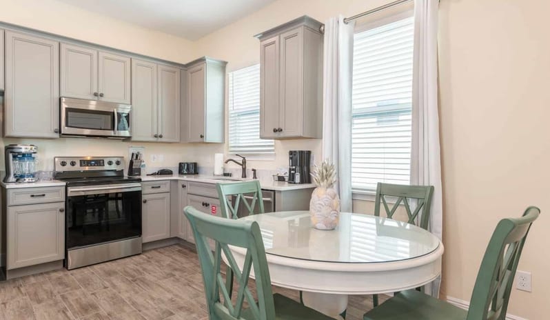 Two Bedroom Villa Kitchen with grey cabinetry and appliances next to a round dining table with green chairs at Margaritaville Resort Orlando by Kenwood Travel