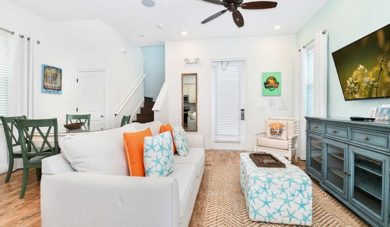 Two Bedroom Villa Spacious open living room with a white couch, patterned ottoman, blue media console, and dining setup at Margaritaville Resort Orlando by Kenwood Travel