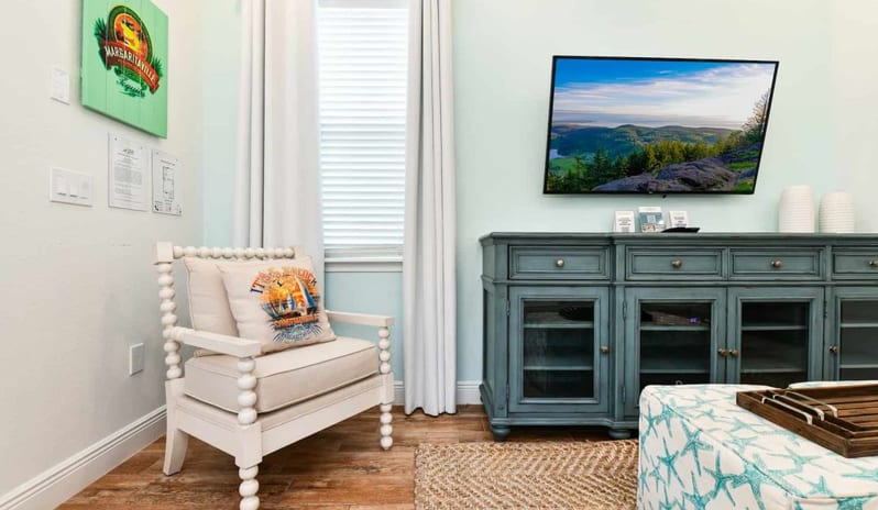 Two Bedroom Villa Accent seating nook in a living room next to a blue media console with a wall-mounted TV at Margaritaville Resort Orlando by Kenwood Travel
