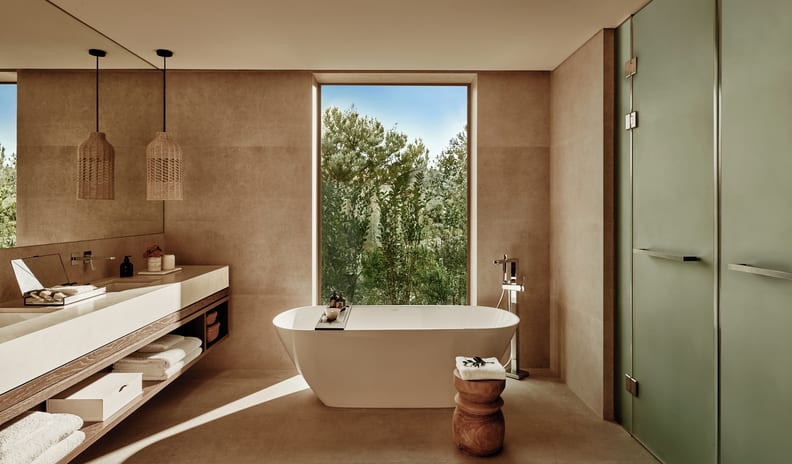 Deluxe Three Bedroom Suite Private Garden Pool View Earthy neutral resort bathroom with a freestanding tub and picture window at Ikos Kissamos by Kenwood Travel