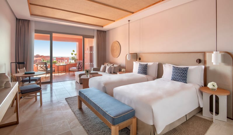 Citadel Two Bedroom Family Resort View Elegantly designed resort bedroom with twin beds, neutral decor accents, a small lounge couch, and direct access to a private terracotta terrace with outdoor seating at Ritz Carlton Tenerife Abama by Kenwood Travel