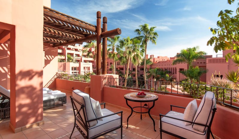 Citadel Two Bedroom Family Resort View Luxury resort terrace with wrought-iron seating, a small round mosaic table, and a shaded outdoor lounge area overlooking a tropical garden courtyard at Ritz Carlton Tenerife Abama by Kenwood Travel