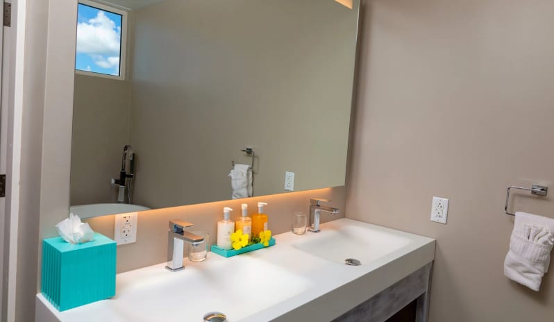 Classic Garden View Modern luxury resort bathroom featuring a double vanity counter with dual undermount sinks, modern chrome faucets, a backlit wall mirror, and tropical bath toiletries at Sea Breeze Beach House by Kenwood Travel