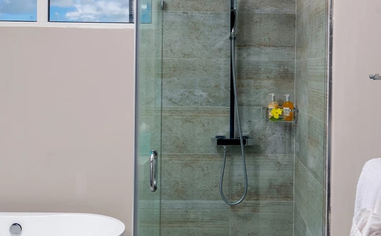 Luxury Suite Two Bedroom Ocean View En-suite hotel bathroom with a frameless glass shower enclosure, a sleek white tub, and a window reflecting a blue sky and palm trees  at Sea Breeze Beach House by Kenwood Travel