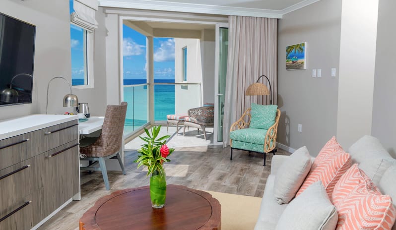 Luxury Suite Two Bedroom Ocean View Coastal hotel suite living area displaying modern wooden cabinetry, a work desk with a woven chair, a woven floor lamp, and a private terrace overlooking the ocean  at Sea Breeze Beach House by Kenwood Travel