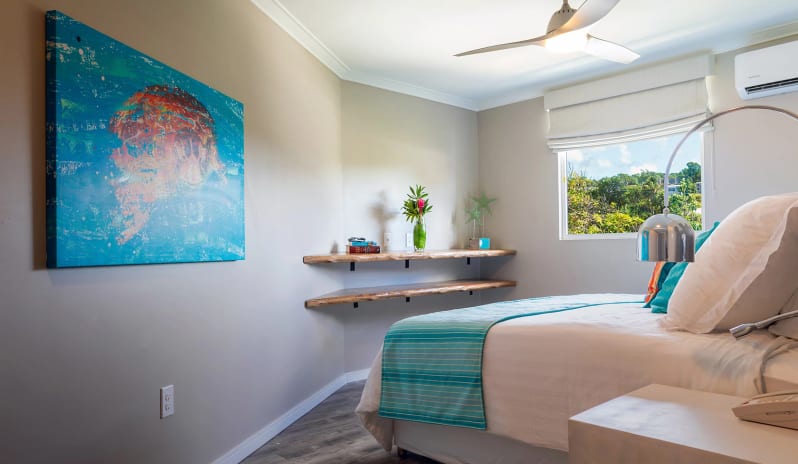 Luxury Suite four Bedroom Ocean Front Coastal resort bedroom interior with light beige walls, a white nightstand, chrome reading lamp, modern ceiling fan, and vibrant turquoise wall decor at Sea Breeze Beach House by Kenwood Travel