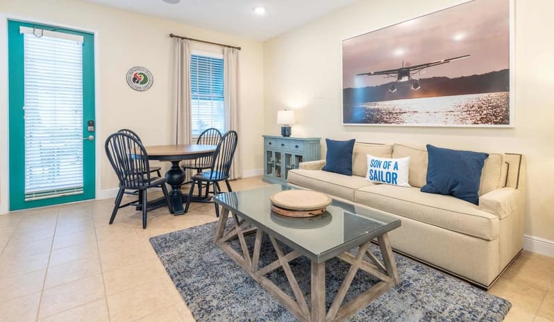 Three Bedroom Villa Cozy living room with sofa, coffee table, and dining table set next to a turquoise door at Margaritaville Resort Orlando by Kenwood Travel