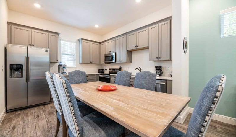 Three Bedroom Villa Large wooden dining table set in front of a modern grey kitchen at Margaritaville Resort Orlando by Kenwood Travel