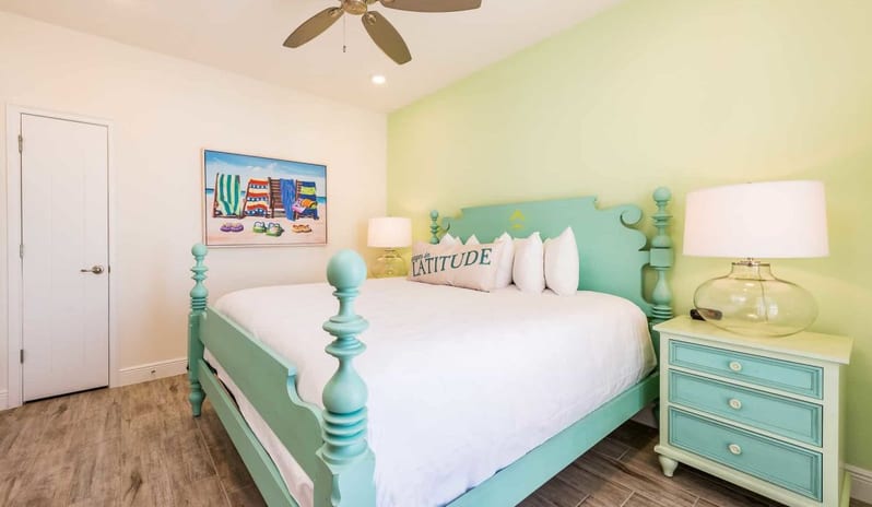 Three Bedroom Villa Tropical bedroom interior with a carved mint green bed frame, lime green accent wall, glass lamp bases, and wood-grain tiled flooring at Margaritaville Resort Orlando by Kenwood Travel