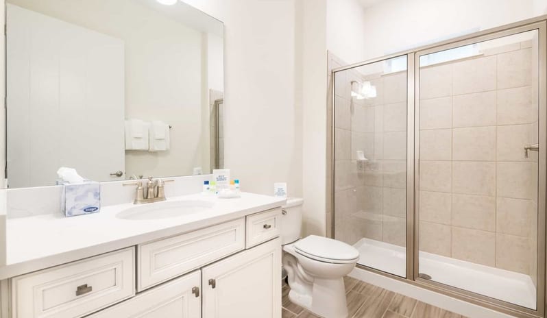 Three Bedroom Villa Clean bathroom layout with a white vanity counter, large mirror, toilet, and glass walk-in shower at Margaritaville Resort Orlando by Kenwood Travel