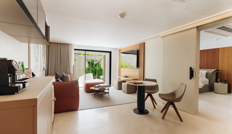 Luxury Pool Suite Modern suite interior showcasing a small marble-top dining table, kitchenette, leather lounge seating, and sliding room partition at Blue Monkey Hotel & Beach Club by Kenwood Travel