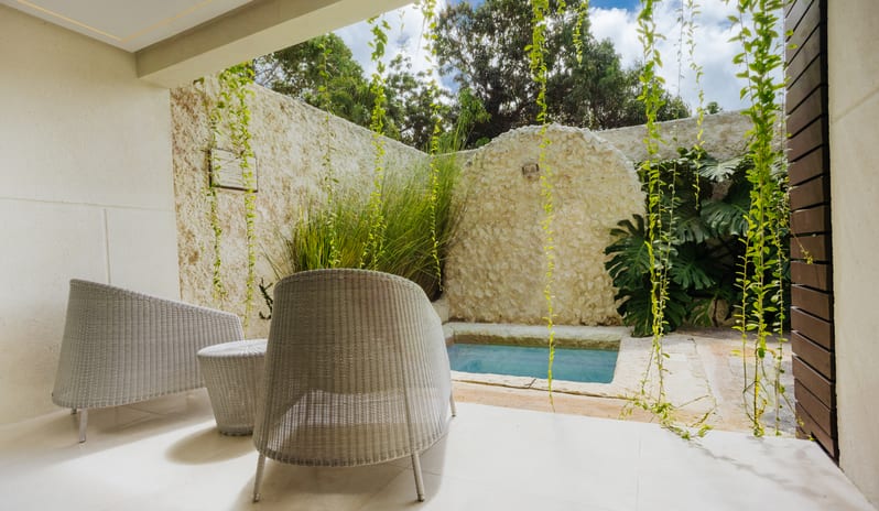 Luxury Pool Suite Modern covered terrace design with wicker seating, hanging vines, a natural stone feature wall, and a small outdoor pool at Blue Monkey Hotel & Beach Club by Kenwood Travel