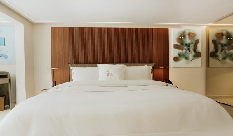 Luxury Two Bedroom Luxury hotel king bed with crisp white linens, plush pillows, slatted wooden headboard accent wall, and ambient lighting at Blue Monkey Hotel & Beach Club by Kenwood Travel