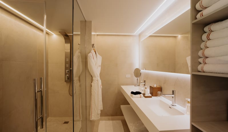 Luxury Pool Suite Modern bathroom interior with seamless neutral tiling, sleek floating vanity, LED strip lighting, and a glass shower enclosure at Blue Monkey Hotel & Beach Club by Kenwood Travel