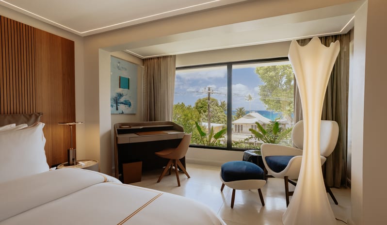 Luxury Pool Suite Modern bedroom interior design with sleek wooden wall paneling, a desk nook, and a tall sculptural floor lamp at Blue Monkey Hotel & Beach Club by Kenwood Travel