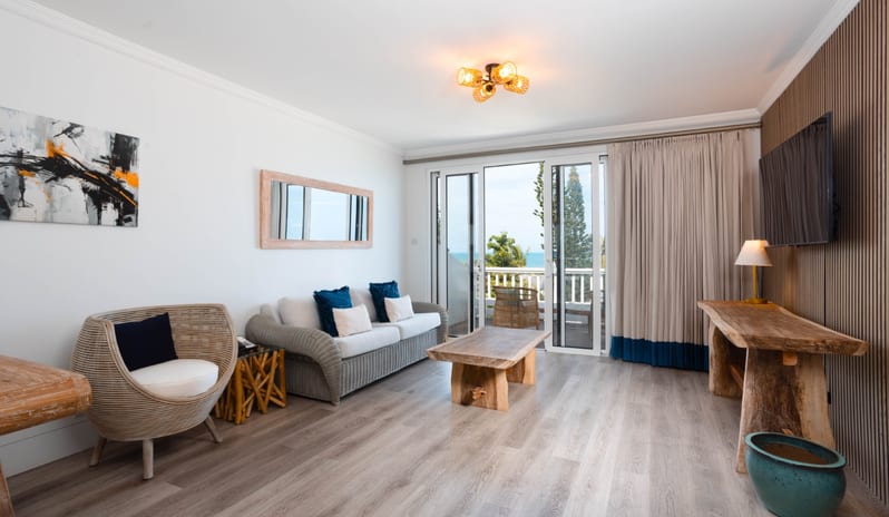 Hillside Luxury Contemporary coastal living room design featuring wood-slat accent wall, rustic wooden console table, woven basket chair, and neutral tones aat Blue Waters Resort & Spa by Kenwood Travel