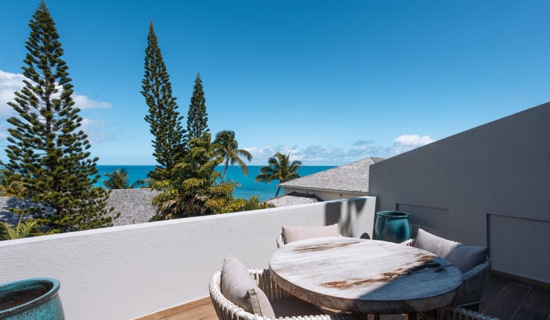 Hillside Luxury Luxury resort suite balcony with outdoor dining table, comfortable patio seating, and panoramic tropical ocean views at Blue Waters Resort & Spa by Kenwood Travel