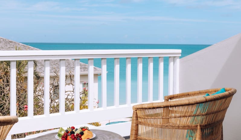 Hillside Luxury Room oceanfront resort private balcony with outdoor seating and fresh fruit platter served against a clear blue sea backdrop at Blue Waters Resort & Spa by Kenwood Travel